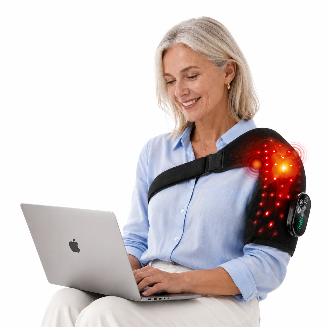 Äldre kvinna använder axelbälte med rödljusterapi och vibration medan hon arbetar vid laptop på vit bakgrund.