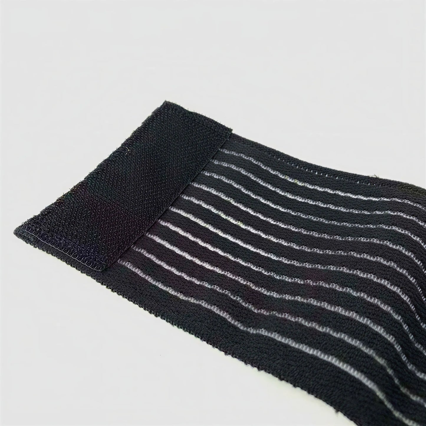 Närbild av elastiskt fotledsband i svart och grått med randig, följsam materialstruktur.