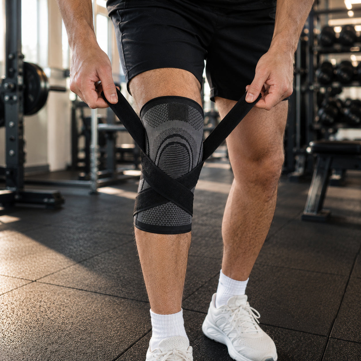 Man justerar ett knäskydd med kompression och spännremmar på gym för extra stöd och stabilitet vid träning.