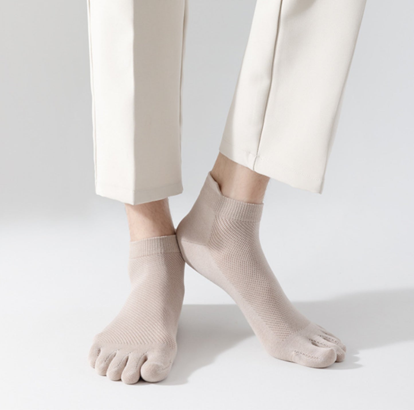 Person står på ljus bakgrund med tunna tåstrumpor i mjukt, följsamt material som separerar tårna och sitter tätt runt foten